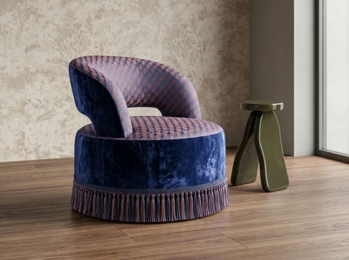 Modern accent chair in blue velvet with patterned upholstery and fringe base, paired with a sculptural metallic side table in a contemporary interior.